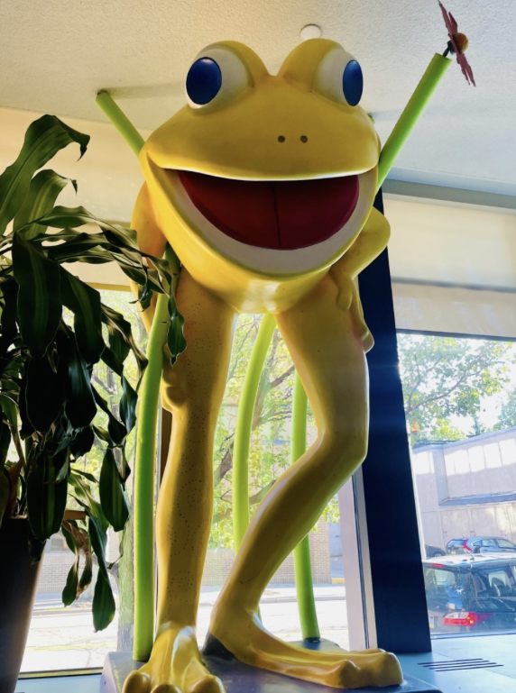 An unnamed frog statue that is bright yellow with tiny holes in a swirl pattern on the legs overlooking Gannon students eating in the cafeteria.